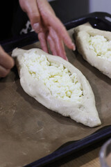 Woman folding dough into a boat shape, shredded suluguni cheese on the dough, preparing a Georgian cuisine dish, khachapuri. Close-up