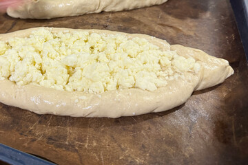 Dough shaped like a boat on a baking tray before baking, topped with shredded suluguni cheese, preparing a Georgian cuisine dish, khachapuri, close-up