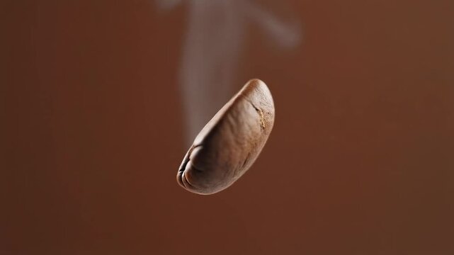 Macro slow-motion video of a single roasted coffee bean floating and rotating with a wisp of steam against a warm brown background
