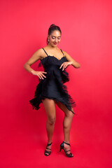 Woman enjoying a lively salsa dance in a black fringe dress on a red background