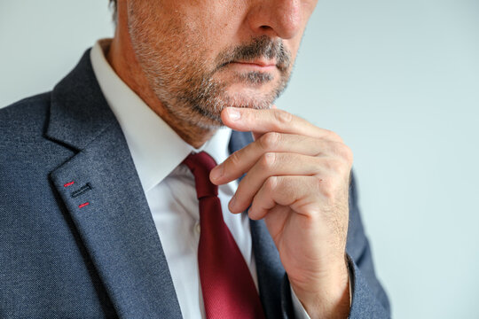 Businessman contemplating strategy with hand on chin, thoughtful office moment. Pensive executive reflecting on business ideas, professional planning indoors.