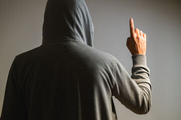 Rear view of man in hoodie raising index finger as if pointing or clicking on invisible virtual screen, tech concept.