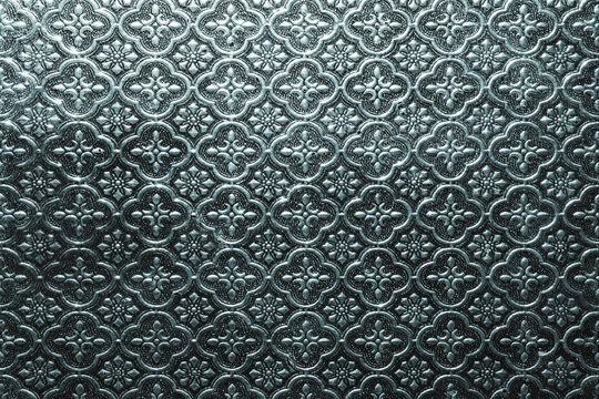 Ornamental patterned glass surface with embossed floral motifs and metallic tone