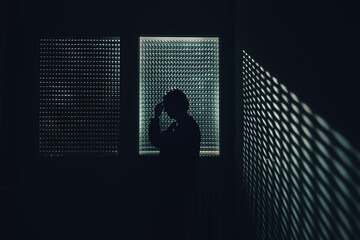 Moody silhouette of a female figure touching forehead near shuttered window with patterned light,...