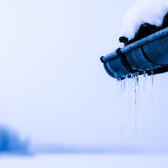 Frozen icicles clinging to metal gutter under pale Nordic winter light