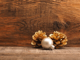 Golden pine cones with a silver Christmas bauble on a wooden background