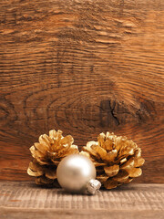 Golden pine cones with a silver Christmas bauble on a wooden background