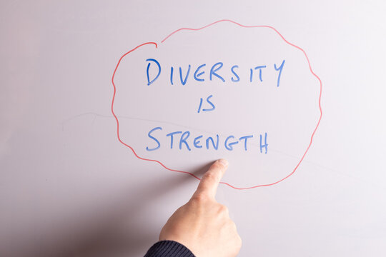 An HR business professional is pointing to the phrase Diversity is Strength on a whiteboard in blue marker pen, ideal for HR, DEI, recruitment, and business workplace presentations.