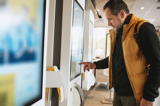 Man using self-service touchscreen kiosk in modern restaurant, interacting with digital ordering system, choosing items on interactive display, concept of technology, automation, and customer convenie