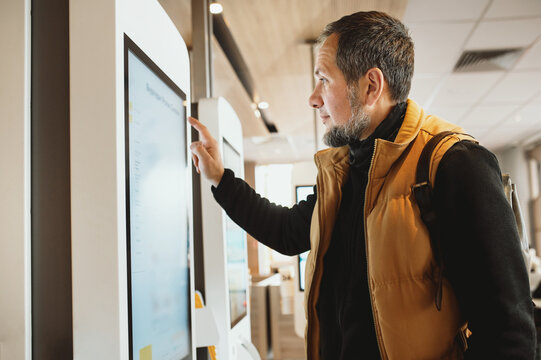 Man using self-service touchscreen kiosk in modern restaurant, interacting with digital ordering system, choosing items on interactive display, concept of technology, automation, and customer convenie