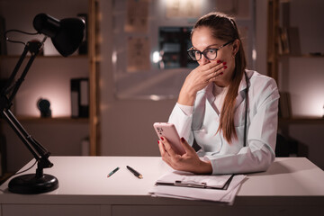 Omg concept. young doctor being deeply surprised looking on smartphone reads shocking news