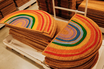 Bright doormats with rainbow design stacked neatly on a store pallet. The concept represents joy,...