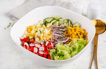 Salad with cabbage, crab sticks, eggs, cucumber and red onions in white bowl. Healthy salad.