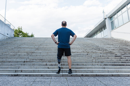 Male athlete with prosthetic leg standing at the bottom of outdoor stairs, preparing for a workout and running challenge.