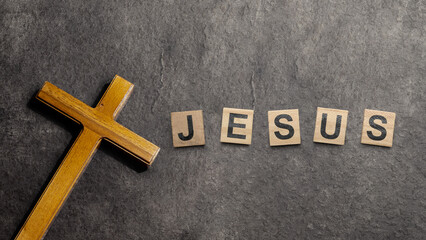 Christian cross and wooden cubes with Jesus text on a black background. Concept of Christianity,...