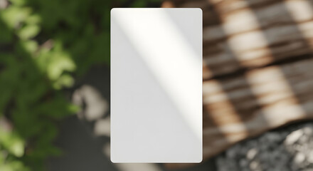Blank white rectangular box mockup casting a shadow on a textured wooden surface with blurred green foliage in the background
