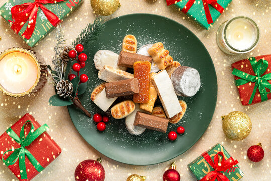 Top view of nougat Christmas sweet,mantecados and polvorones on a green plate with Christmas ornaments. Assortment of Christmas sweets typical in Spain