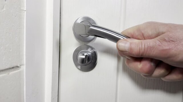 Closeup slow motion shot of a man&rsquo;s hands holding a handle while pulling an internal door closed, then  turning a locking mechanism to secure it.