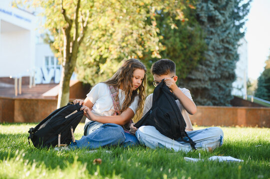 School children packing backpacks on grass after lessons