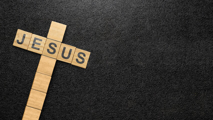 Wooden cubes with Jesus text and a Christian cross pattern on a black background. Concept of Christianity, religious, faith, Jesus, or belief