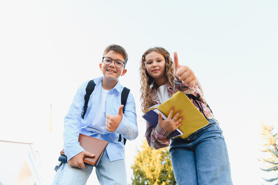 Happy schoolchildren giving thumbs up gesture outside school