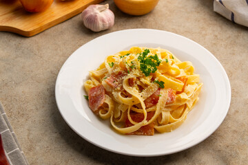 Creamy fettuccine pasta with bacon and carbonara sauce topped with parsley and parmesan cheese in a plate.