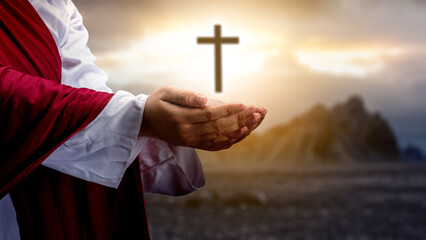 Jesus Christ raising his hand and praying with the Christian cross on the hill with dark dramatic...