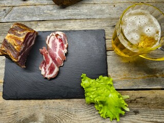 Beer snack on a granite cutting board, with slices of cheese, smoked ham, salad and side dishes laid out on it, and a glass of beer.