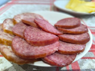 Close-up of thinly sliced salami on a white plate, garnished with rosemary sprigs.