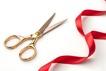 Macro gold scissors and scarlet ribbon on white background