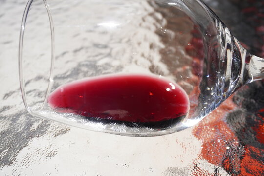 Close-up of a tilted wine glass with a small amount of red wine resting inside. The light highlights the deep ruby color and reflections on the clear glass, creating a refined and elegant composition.