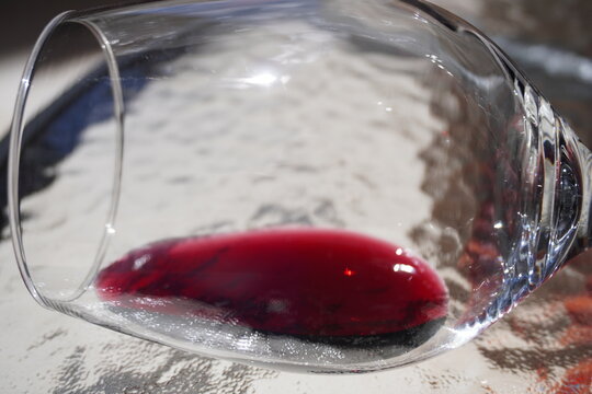 Close-up of a tilted wine glass with a small amount of red wine resting inside. The light highlights the deep ruby color and reflections on the clear glass, creating a refined and elegant composition.