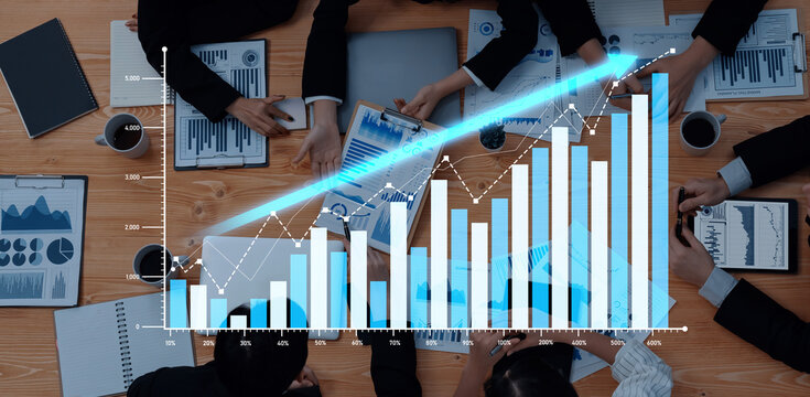 A top view of business professionals engaged in strategic discussions, utilizing graphs and data visualizations to illustrate market trends and growth opportunities in a dynamic office setting. Scalp