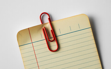 Closeup of a red paperclip holding a lined index card on a white surface creating a simple yet visually appealing composition perfect for office supplies and organizational themes