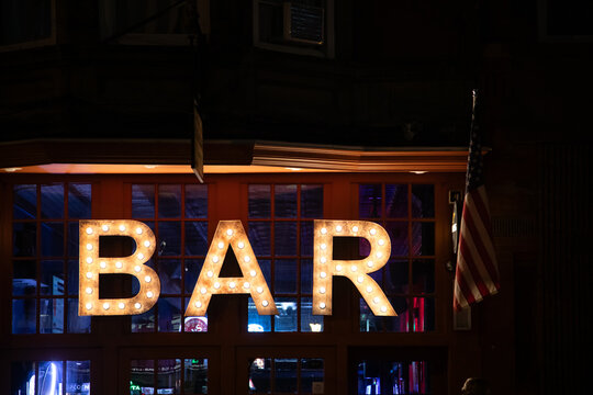 Bright bar sign lights up the street at night in a vibrant urban setting