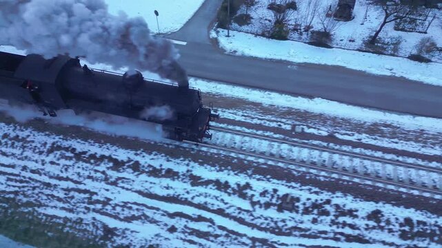 Steam train puffs and speeds through a snowy landscape. This historic means of transport, seen by a drone, travels through a snowy Trentino valley in winter