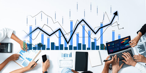 A diverse team engages in a business meeting, analyzing financial data and trends on digital devices, showcasing collaboration and strategic planning in a modern workspace. Scalp