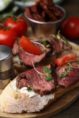 Delicious bruschettas with roast beef served on wooden table, closeup