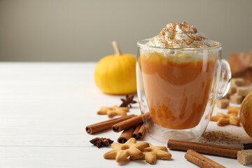 Tasty pumpkin latte with whipped cream in glass cup, cookies and ingredients on white wooden table, closeup. Space for text