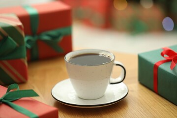 Aromatic coffee in cup and gift boxes on wooden table, closeup. Christmas greeting card