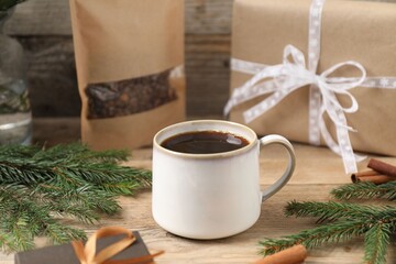 Aromatic coffee in cup, beans, gift boxes and fir tree branches on wooden table, closeup. Christmas...
