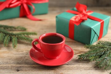 Aromatic coffee in cup, gift boxes and fir tree branches on wooden table, closeup. Christmas...