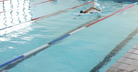 Swimming woman freestyling at aquatic pool, lane dividers, in one-piece, cap, goggles, copy space