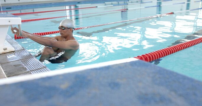 Gripping starting block handles, swimmer in silver cap and goggles bracing at pool, copy space