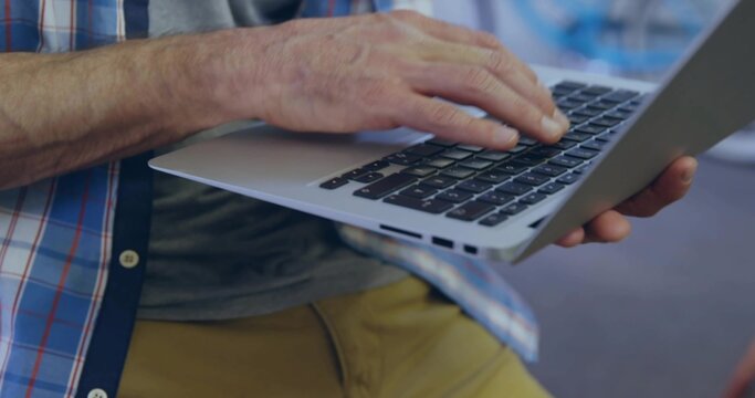 Typing mature man wearing plaid shirt and mustard pants, using slim silver laptop in lounge