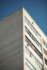 Close-up of old Soviet style residential apartment facade with brick and metal panels against blue sky.