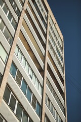 Upward view of tall residential block with balconies and windows under clear sky, concept of urban life and architecture.