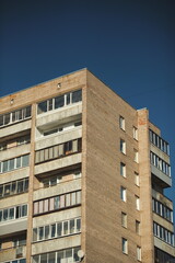 Close-up of old Soviet style residential apartment facade with brick and metal panels against blue sky.