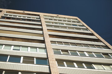 Close-up of old Soviet style residential apartment facade with brick and metal panels against blue sky.