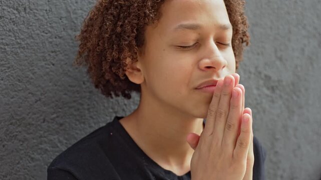 Young Person Against Textured Wall With Hands Together And Eyes Closed In Prayer  During Moment Of Calm And Spiritual Reflection